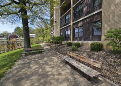An outdoor walkway with two benches and a tree next to a multi-story apartment building.